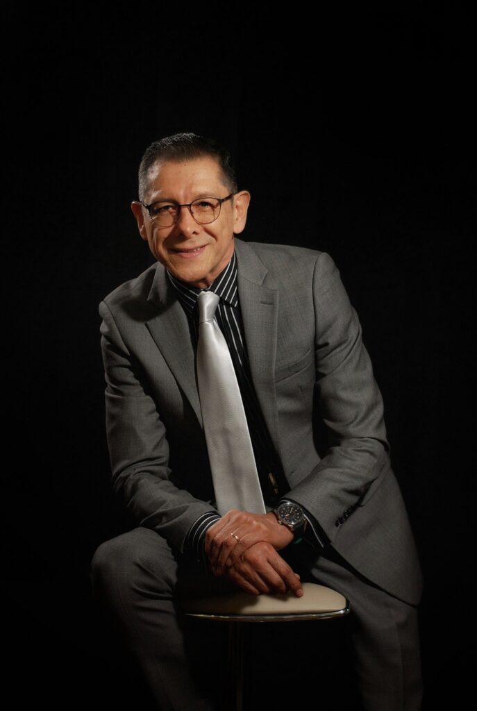 Yesid Barrera, facilitador de desarrollo humano y organizacional de RYBS Ideas, sentado con traje gris